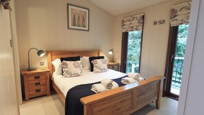 A bedroom with a wooden bed, two bedside tables with lamps, a framed picture on the wall, and a window with curtains. - Beck of Beyond (Ambleside)