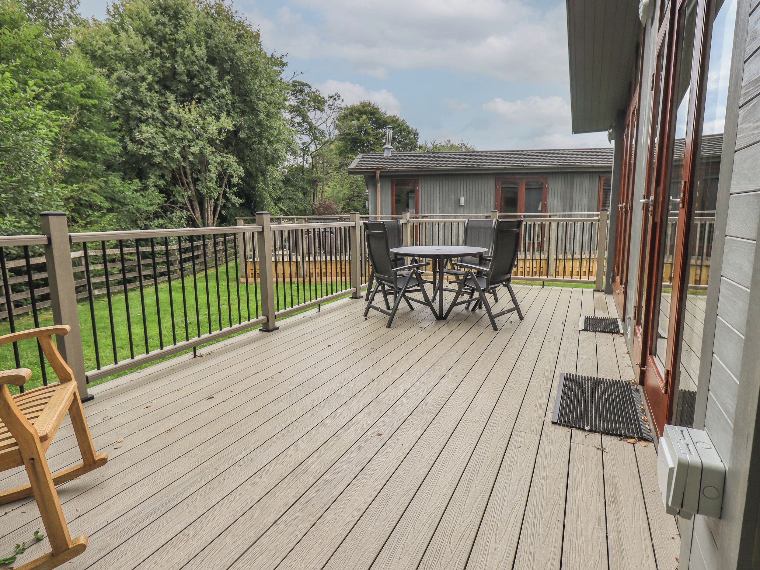 A wooden deck with a table and chairs, a wooden bench, a metal railing, and a view of a house in the background.