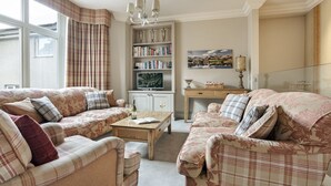 A cozy living room with two sofas, a coffee table, a bookshelf, and a painting on the wall. - Archie's (Ambleside)