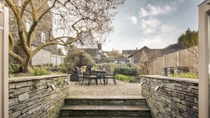 A stone staircase leading to a patio area with a table and chairs, surrounded by a stone wall and a garden. - Archie's (Ambleside)