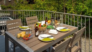 Un tavolo da pranzo all'aperto apparecchiato con piatti, posate e diversi cibi, circondato da ringhiere metalliche e vegetazione.