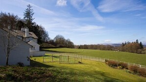 A white house with a fenced yard and a green field with sheep. - Juniper Cottage (Windermere)