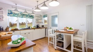 A modern kitchen with white cabinetry, a wooden countertop, and a dining area with white chairs. - Juniper Cottage (Windermere)