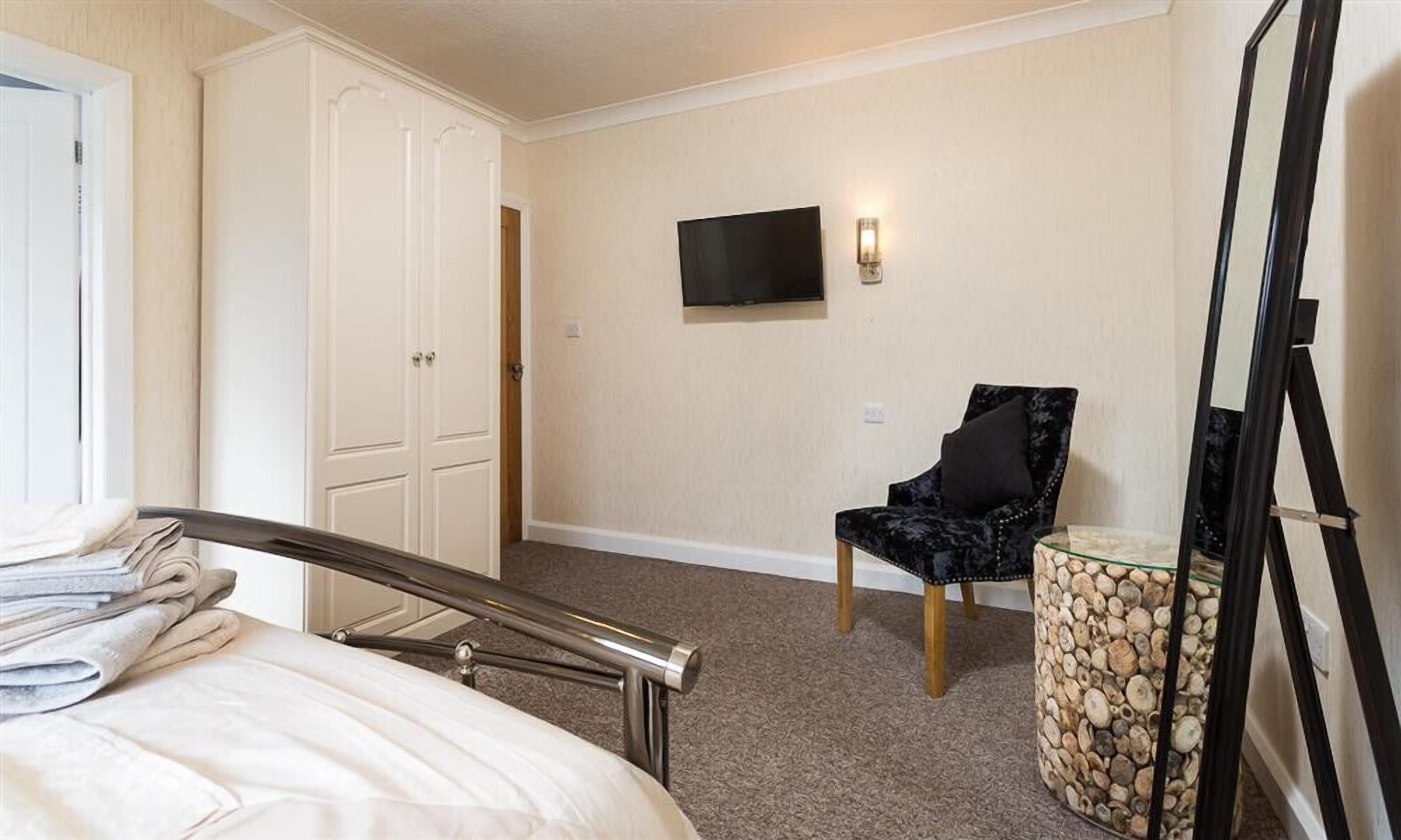 A bedroom with a bed, a chair, a television, and a mirror.