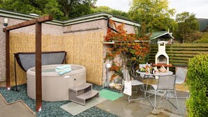Un bain à remous, un espace salon extérieur et un four à pizza, le tout aménagé dans un jardin.