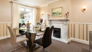 Une salle à manger avec une table en verre, des chaises, une cheminée et un tableau au mur.