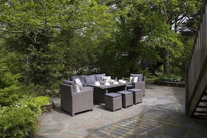 An outdoor patio with wicker furniture and stone flooring, surrounded by lush greenery. - Rosewood by the River (Ambleside)