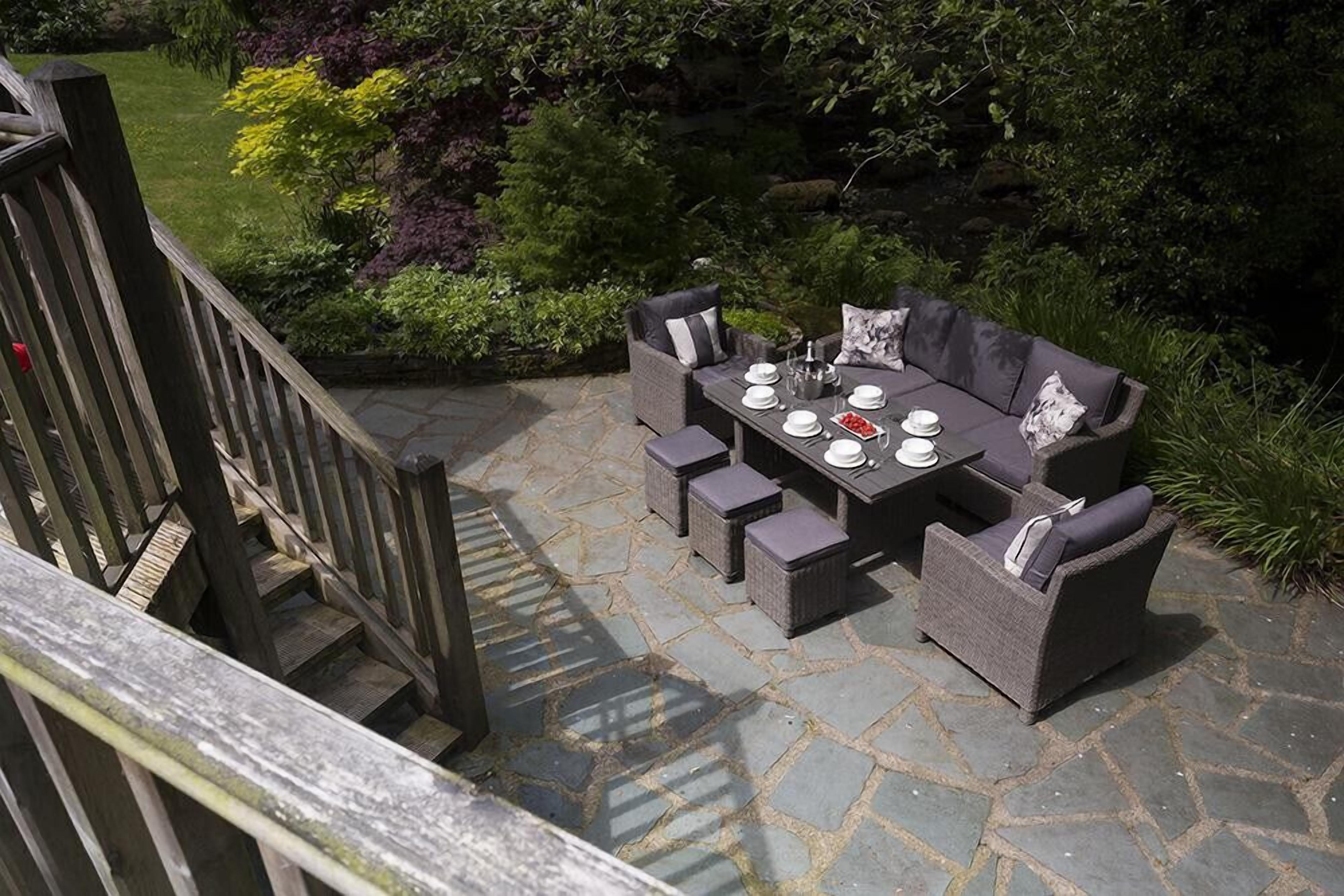 An outdoor patio with a stone table set for dining, surrounded by wicker furniture.