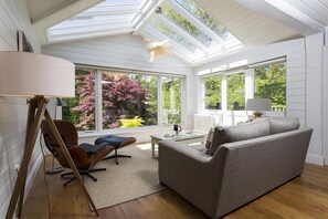 A modern living room with a skylight, large windows, a sofa, a chair, and a coffee table. - Rosewood by the River (Ambleside)