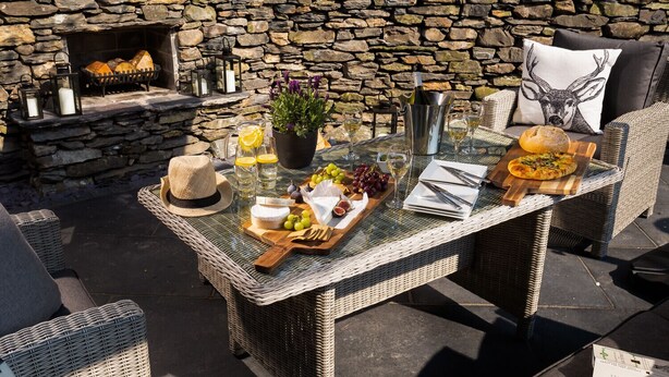 An outdoor dining area with wicker furniture, a stone wall, and a fireplace. - Lexington House (Windermere)
