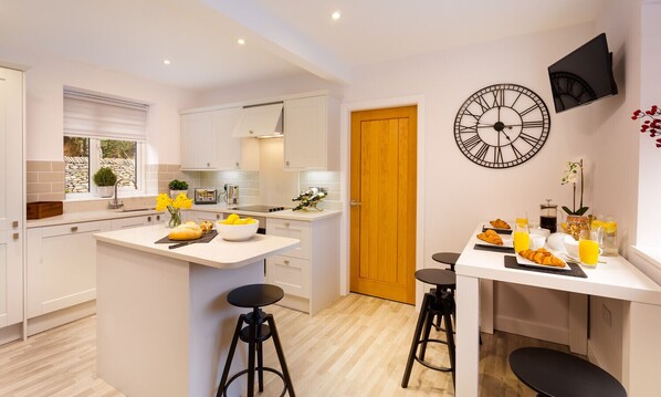 A modern kitchen with white cabinetry, a central island with stools, a wooden door, and a wall-mounted clock.