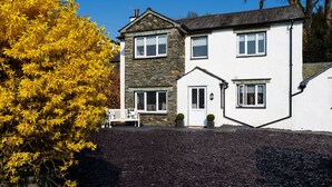 A two-story house with a stone facade and white walls, a front porch with a bench, and a small garden area with yellow foliage. - Lexington House (Windermere)
