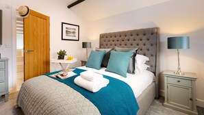 A neatly arranged bedroom with a large bed, bedside tables, a bedside lamp, a door, and a framed picture on the wall. - Lexington House (Windermere)