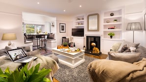 A modern living room with a fireplace, a dining area, and a TV. - Lexington House (Windermere)