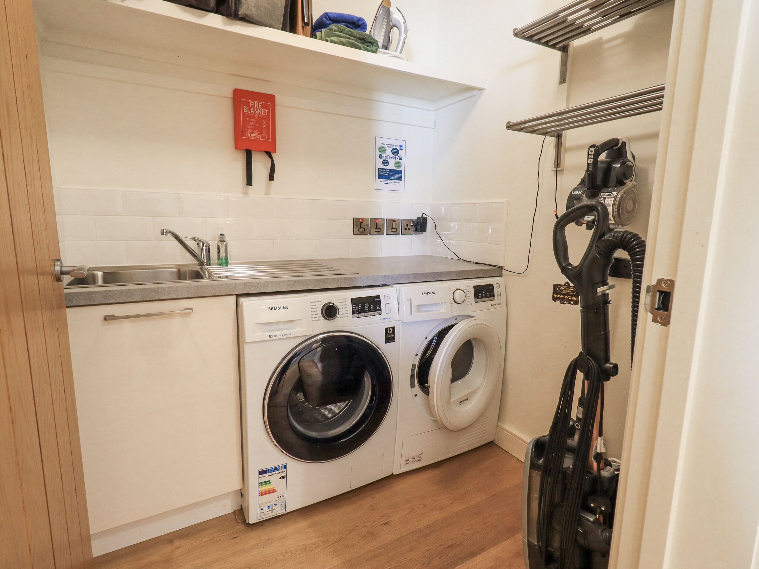 A compact kitchen with a washing machine, a sink, and a fire blanket on the wall.