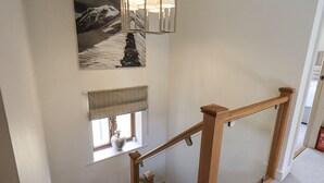 A staircase with a wooden handrail and a glass balustrade, a window with a view of a mountain, and a wall-mounted light fixture.