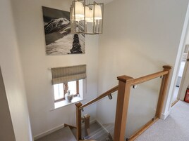 A staircase with a wooden handrail and a glass balustrade, a window with a view of a mountain, and a wall-mounted light fixture.