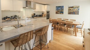 A modern kitchen with a central island, bar stools, wooden dining table, and two paintings on the wall.