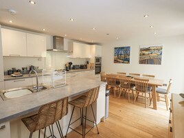 Una cocina moderna con una isla central, taburetes de bar, una mesa de comedor de madera y dos cuadros en la pared.