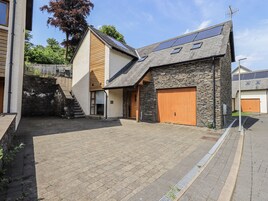 A modern house with a stone facade, a wooden door, and a paved driveway.