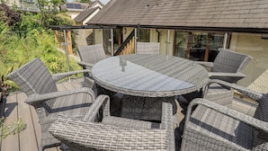 An outdoor patio with a round table and wicker chairs, surrounded by glass railings.