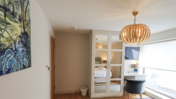 A modern bedroom with a bed, a large window, a hanging light fixture, and a painting on the wall.