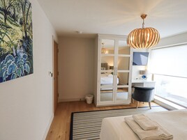 A modern bedroom with a bed, a large window, a hanging light fixture, and a painting on the wall.