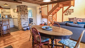 A cozy dining area with a wooden table and chairs, a stone pillar, and a staircase leading to another level.
