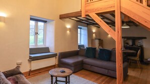 A cozy living room with a wooden staircase, a sofa, a coffee table, and a window with a view.