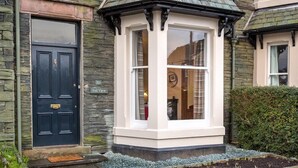 A house with a black door, a stone facade, and a bay window with a white trim. - Thirty Blencathra Street (Keswick)