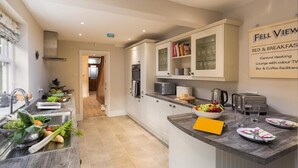 A modern kitchen with a central island, built-in appliances, and a view sign indicating amenities like bed & breakfast, central heating, and tea & coffee facilities. - Thirty Blencathra Street (Keswick)