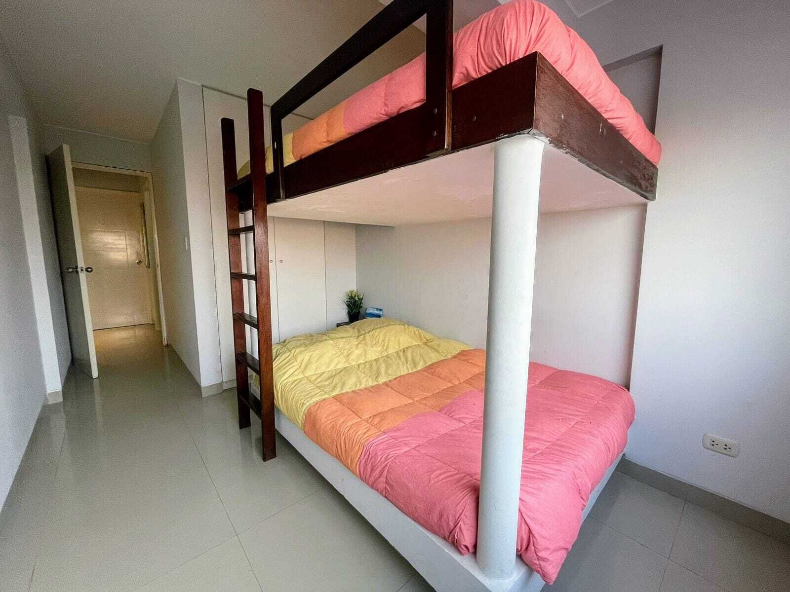 Un lit superposé avec une échelle, une table de chevet et une porte à l’arrière-plan.