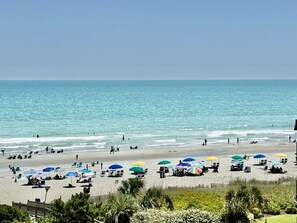 Een strand met parasols en ligbedden, een heldere lucht en de oceaan.