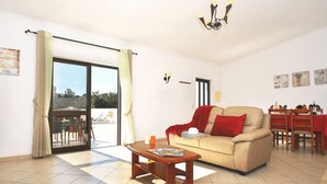 A living room with a sofa, a coffee table, a dining area with a table and chairs, and a sliding glass door leading to an outdoor space. - Rustic retreat w/ private pool, Guia (Albufeira)