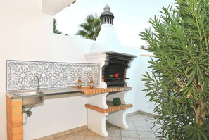 An outdoor kitchen area with a tiled backsplash, a sink, and a grill.