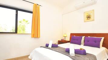 A hotel room with a bed, a nightstand, a lamp, a window with curtains, and an air conditioning unit.