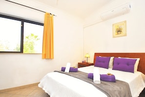 A hotel room with a bed, a nightstand, a lamp, a window with curtains, and an air conditioning unit.