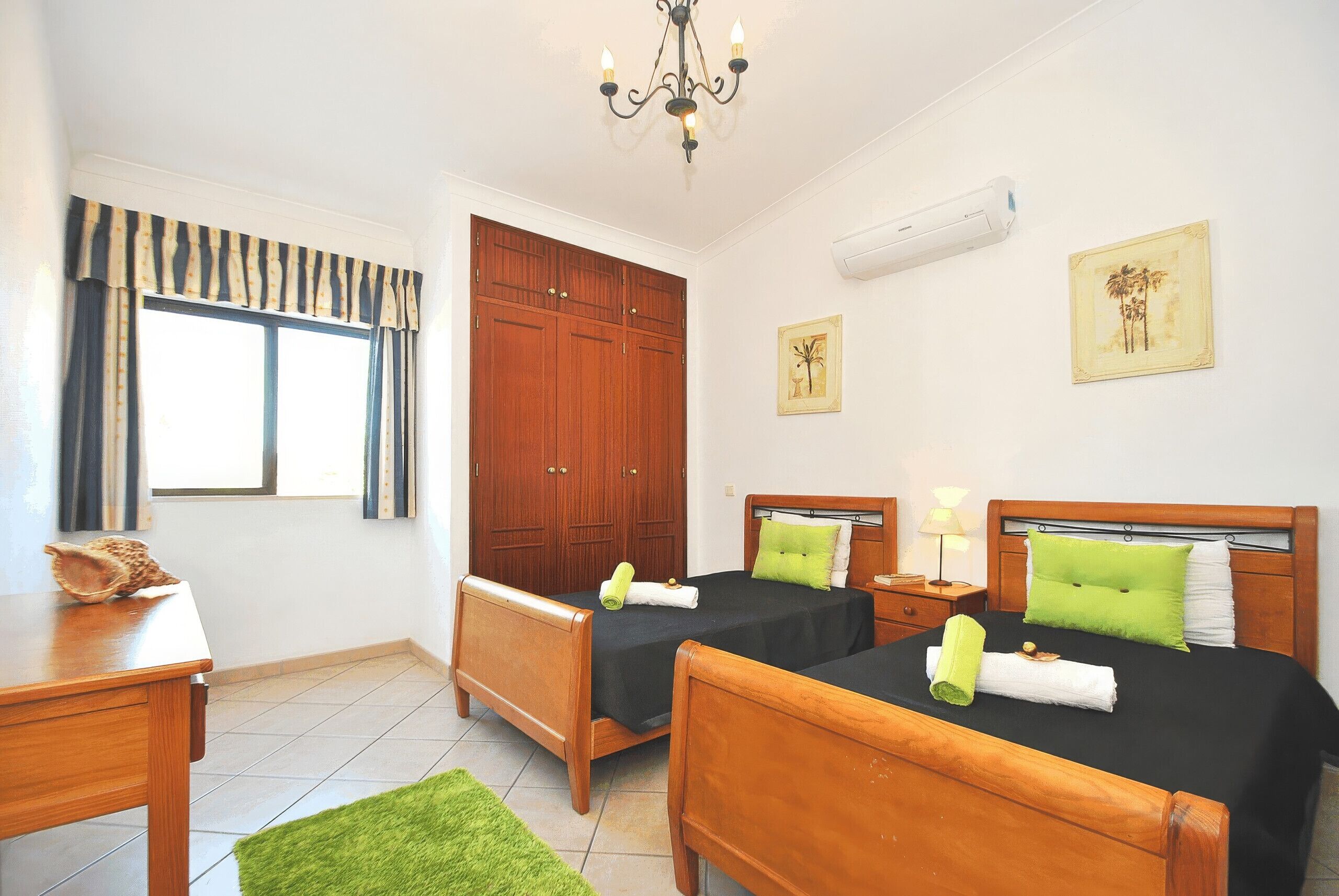 A hotel room with two beds, a wooden wardrobe, a chandelier, and artwork on the walls.