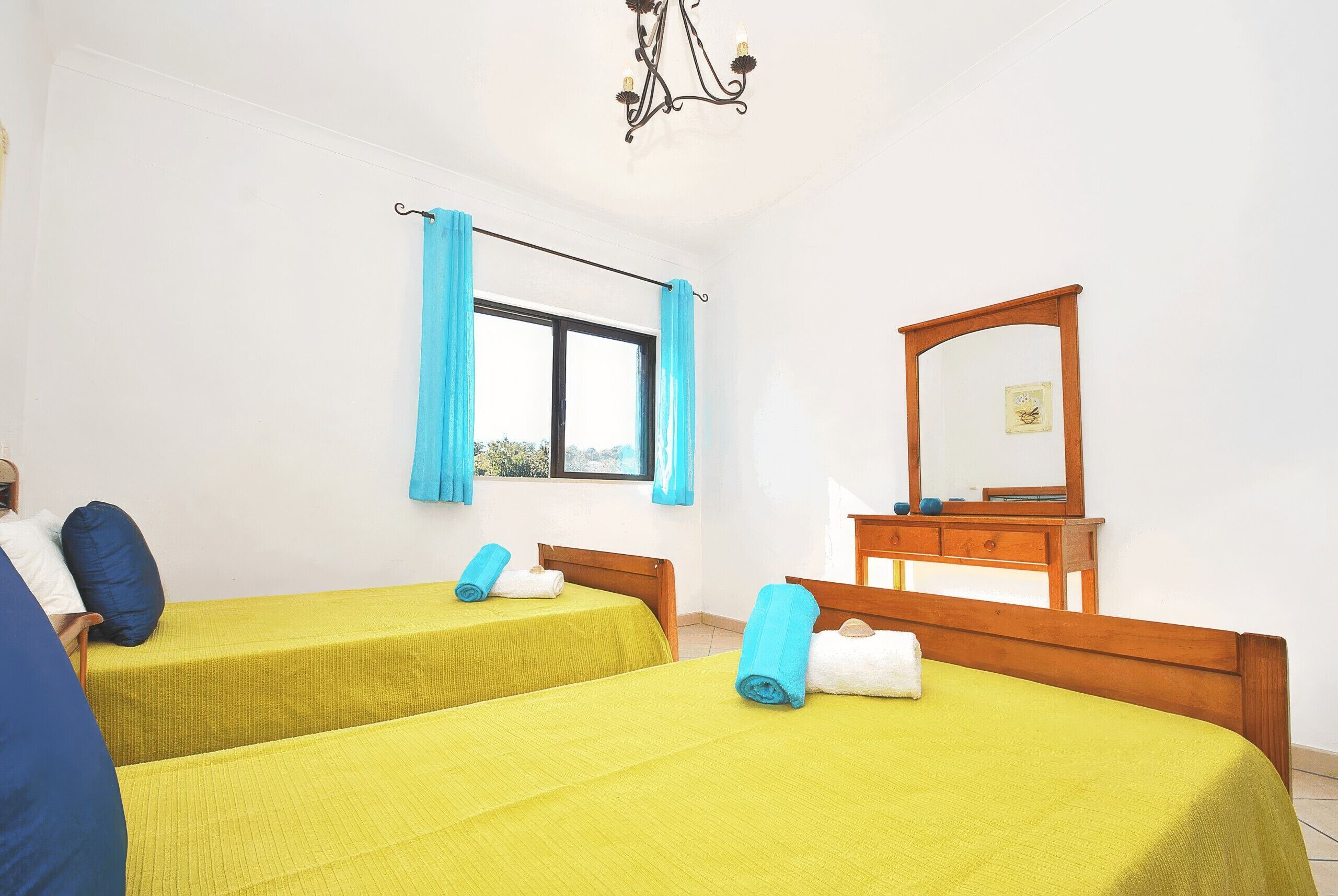 A hotel room with two beds, a wooden dresser, a mirror, and a window with curtains.