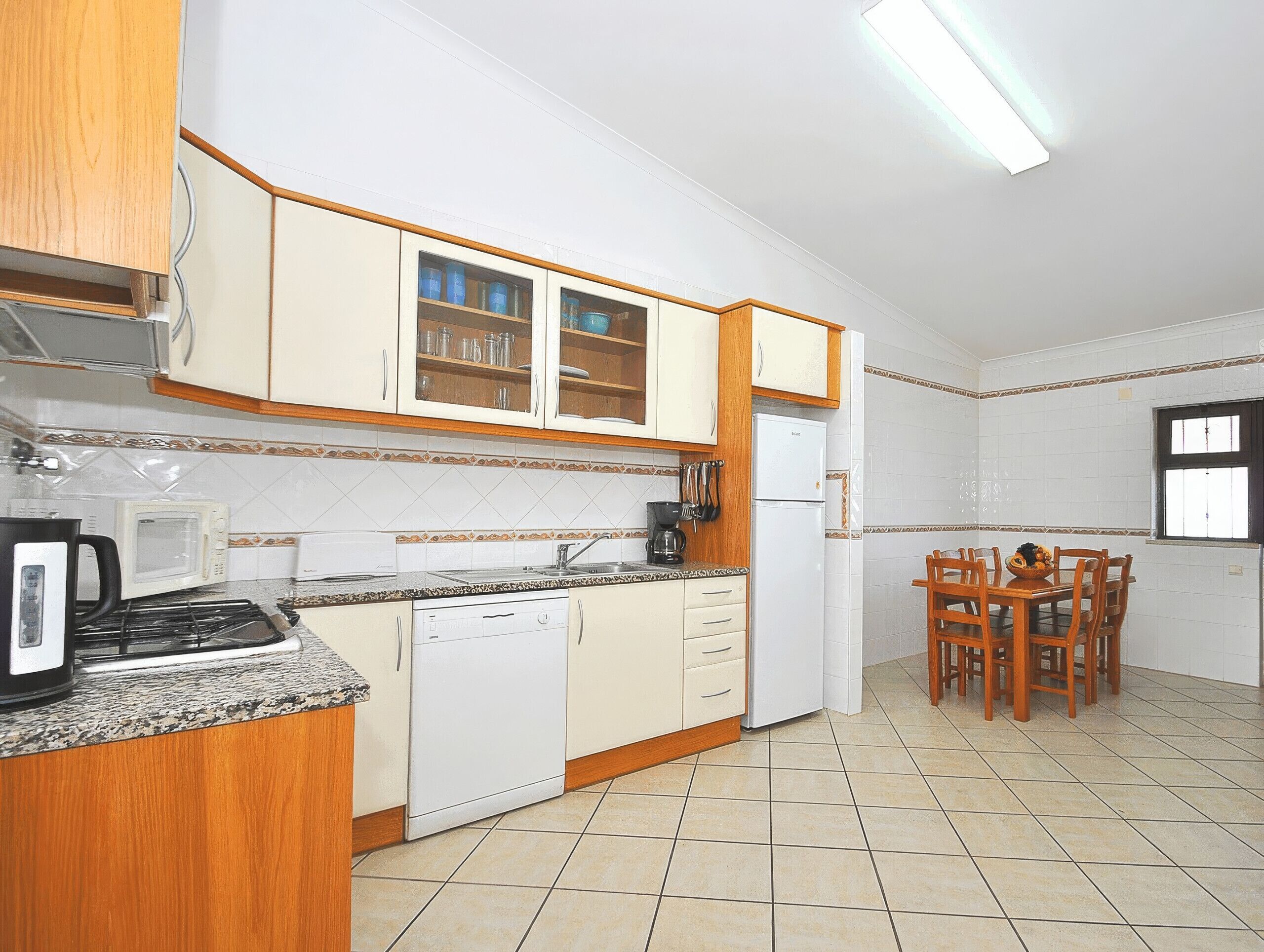 A kitchen with wooden cabinets, a microwave, a coffee maker, and a dining table with chairs.