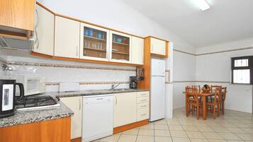 A kitchen with wooden cabinets, a microwave, a coffee maker, and a dining table with chairs.