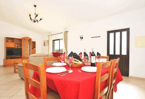 Un coin repas avec une nappe rouge, des chaises en bois et un lustre.