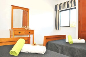 A hotel room with a wooden dresser, a mirror, two beds with towels, a window with curtains, and a wooden door.