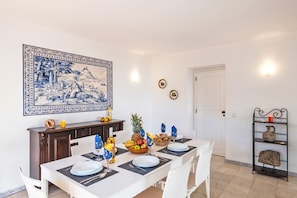 Comedor con una mesa preparada para cuatro, un adorno en la pared y una estantería con objetos.