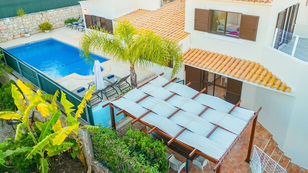 A residential property with a swimming pool, outdoor seating, and a covered patio area.