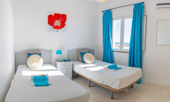 Habitación de hotel con dos camas, una mesita de noche, una lámpara y un ventanal con cortinas.