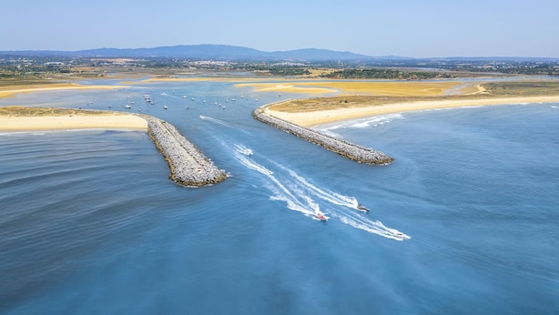 An aerial view of a coastal area with a clear sky, a sandy beach, and a waterway with boats.