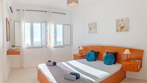 A bedroom with a wooden bed, two bedside tables, a nightstand, a window with curtains, and a wall-mounted artwork.
