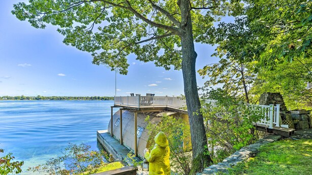A wooden deck overlooking a lake with a stone structure and a yellow statue. - Waterfront Wellesley Island Getaway w/ Deck! (Wellesley Island)