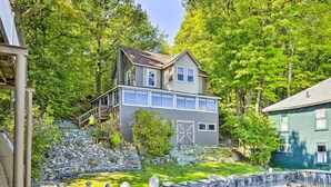 A two-story house with a stone retaining wall and a small pond. - Waterfront Wellesley Island Getaway w/ Deck! (Wellesley Island)